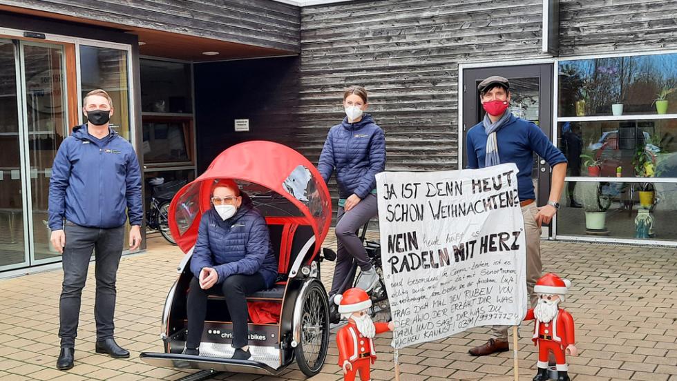 Besetzte Rikscha und ein Banner mit der Aufschrift "Radeln mit Herz" vor einer AWO Einrichtung