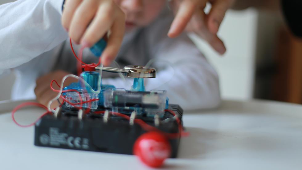 Kita-Kind bei einem Technik-Experiment, unterstützt von einem Erwachsenen